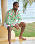 Man seated in Watermelon Green linen shirt with white shorts beside the sea in an island setting