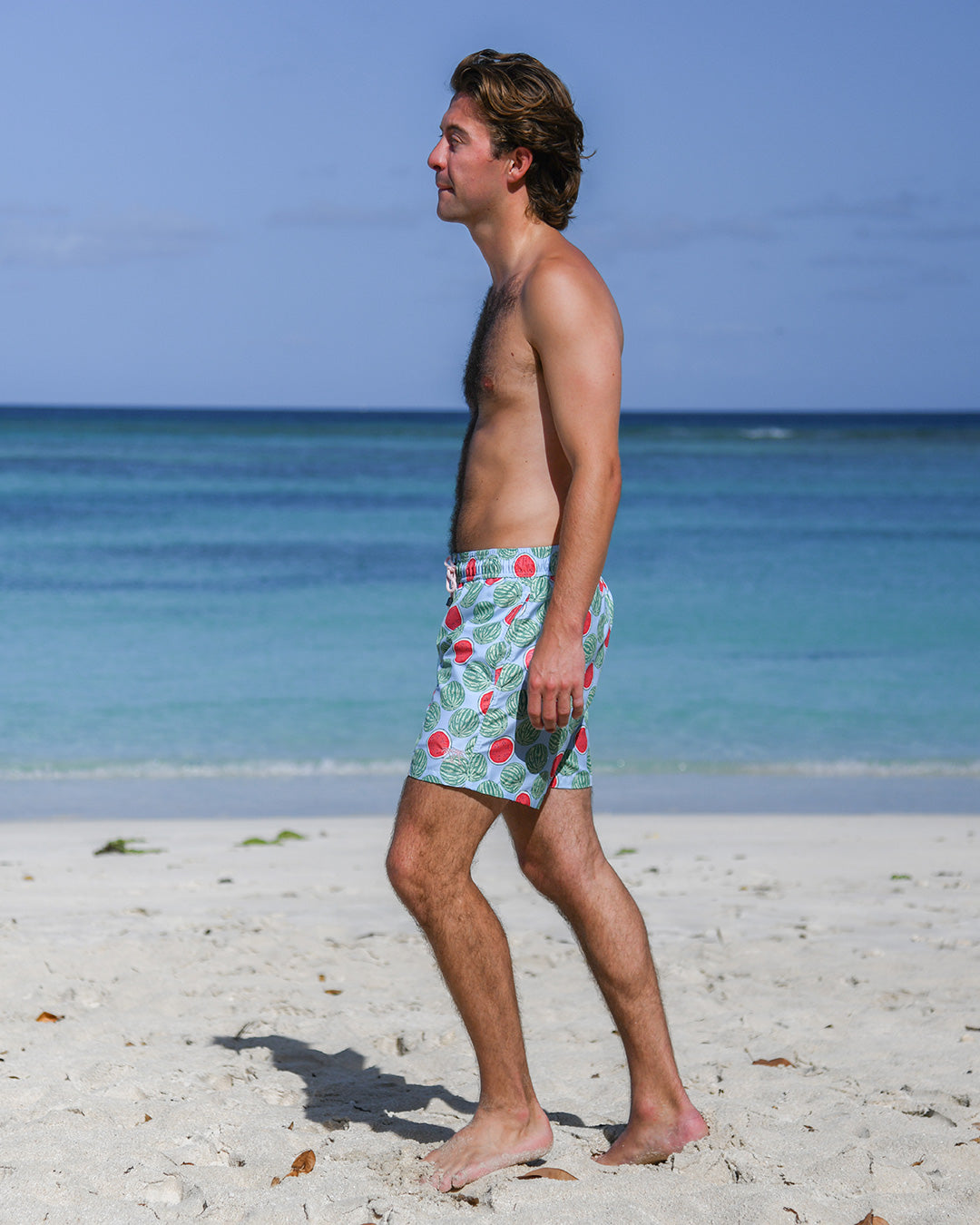 Side view of man wearing Watermelon print men's swim shorts on a tropical beach