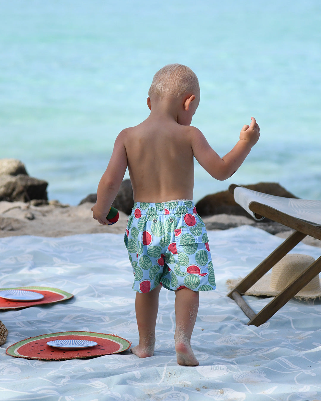 Back view of little boy wearing Watermelon print boys' swim shorts at the beach