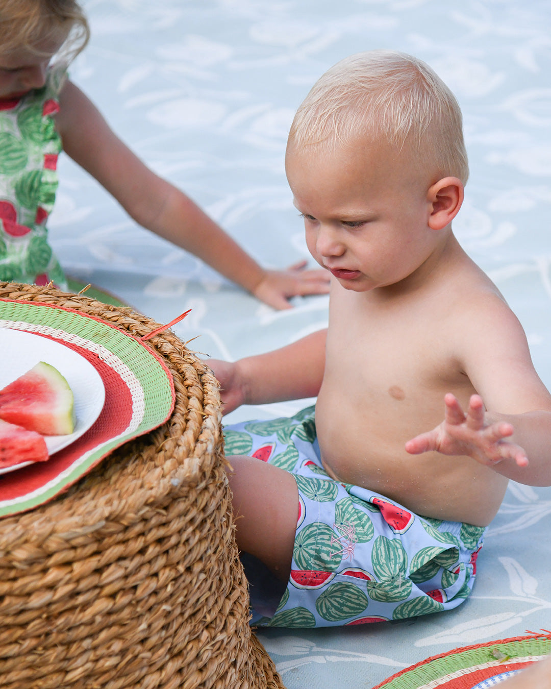 Little boy wearing Watermelon print swim shorts beside fresh watermelon at a beach picnic