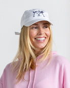 Woman wearing white Mustique Palms logo cap and pink cashmere hoodie smiling