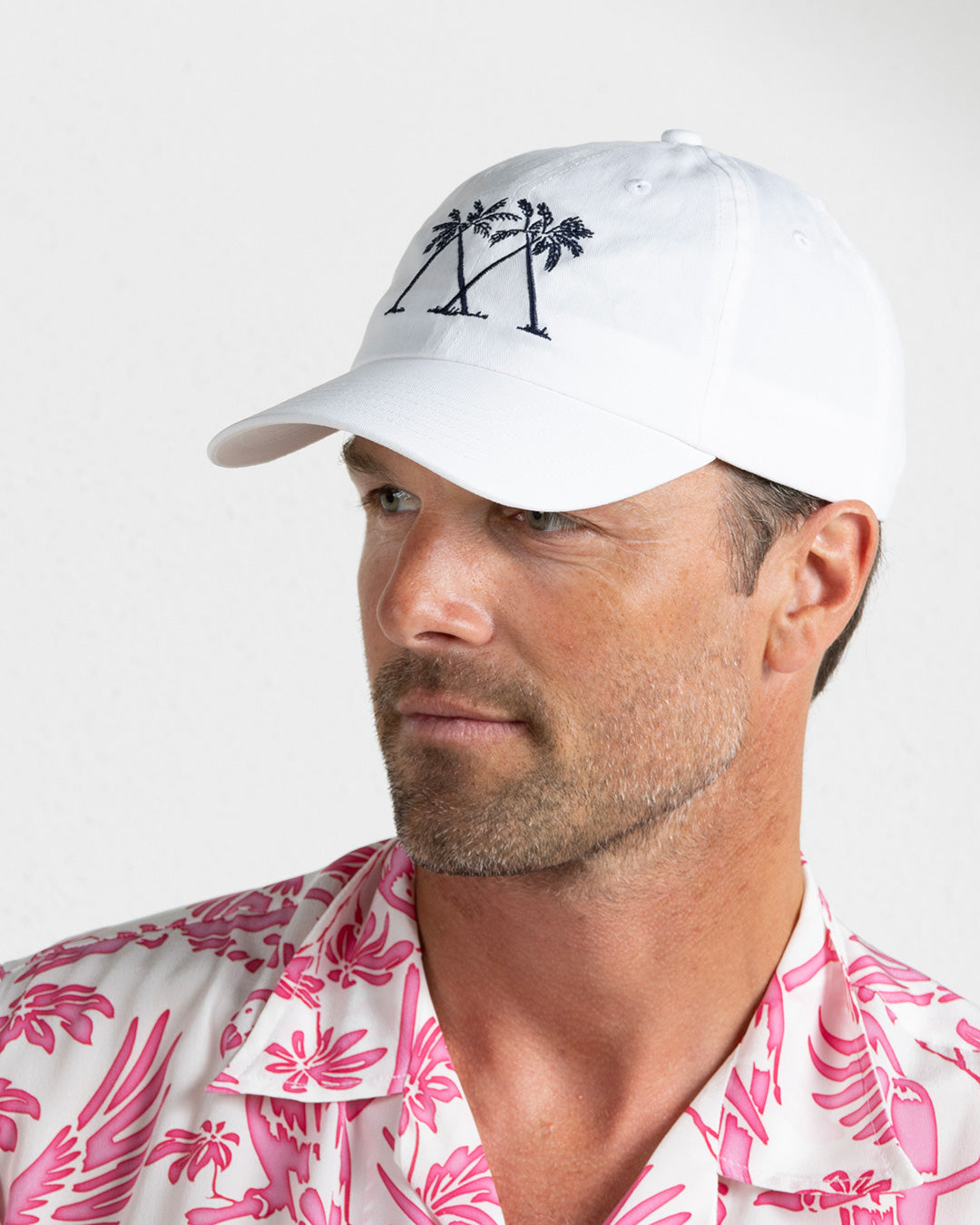 White Mustique Palms baseball cap with navy embroidery worn by Joss in pink silk Parrot shirt