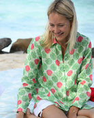 Woman wearing Watermelon Green Anastasia linen shirt with white shorts in a relaxed island setting