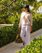 Woman wearing a beige 100% Mongolian cashmere hoodie styled with white linen Flora trousers and navy cap by Pink House Mustique