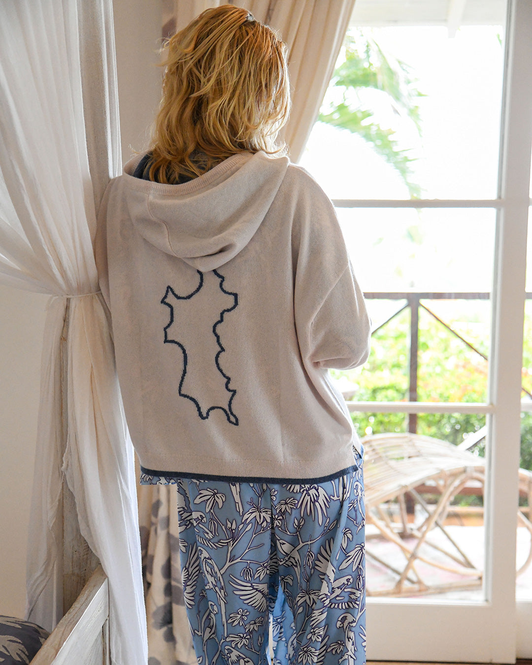Woman wearing a 100% Mongolian cashmere hoodie by Pink House Mustique featuring the outline of Mustique on the back